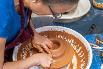 A woman bent over the pottery wheel starting to work the clay to make the clay in a new piece.