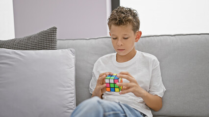 Blond boy sitting on sofa playing with rubik cube at home