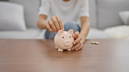 Obraz na płótnie Canvas Adorable boy's hands inserting money into piggy bank while comfortably sitting on a living room sofa at home, symbolizing childhood financial learning