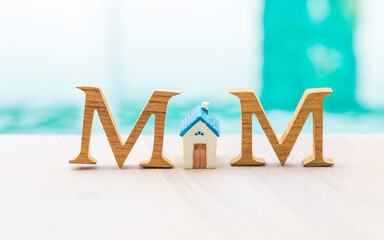 Mother's day card background idea, M wooden alphabet letter with miniature house over blurred background, outdoor day light 