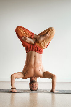 a man with a naked torso does yoga standing on his head indoors. Fitness Trainer