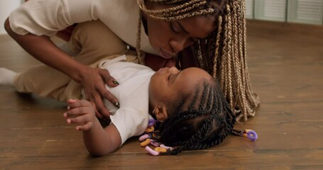 little nice kid lying on floor, Loving tender young mum raising, holding adorable cute girl daughter embracing kissing kid. Happy affectionate mother cuddling with child at home.slow motion