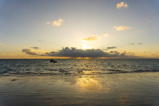Boats off the shore just after Sunrise. Golden hour at the Beach with some Clouds in the Sky iluminated by the Sun.