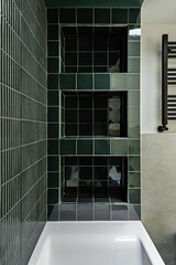 Bathroom of a modern house with white bathtub and bright dark green tiles with a niche with shelves...