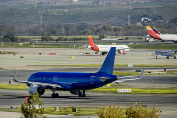 A blue airplane transiting the access runways to the take-off runway at Madrid Barajas airport