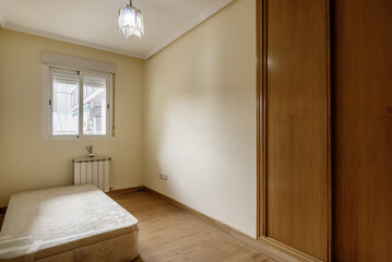 A small empty room with an old folding sofa and a built-in wardrobe with light oak sliding wooden...