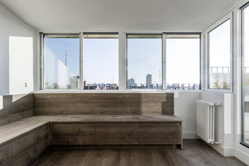 A perimeter wooden bench with drawers under a long window with white aluminum and glass sliding windows
