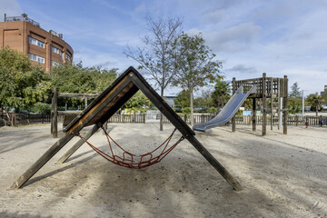 An urban playground with swings and slides and other games on a sandy floor