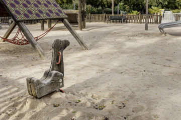 A wooden children's game in the shape of a dromedary head inside a playground with sand floors and wooden games