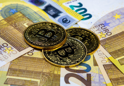 A closeup of Bitcoin coins over Euro banknotes. It represents virtual and real money