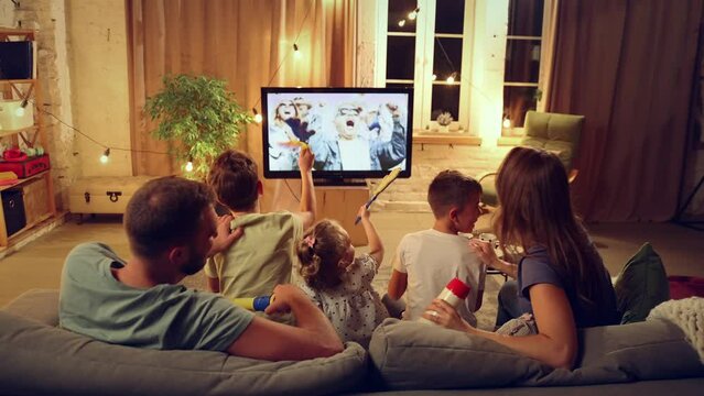 Back view. Family, parents and children sitting on couch in evening at home and watching football match translation. Winning game. Concept of family, leisure time, relaxation, childhood and parenthood