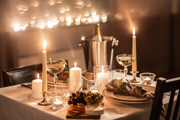 holidays, romantic date and celebration concept - close up of festive table serving for two with champagne bottle in ice bucket and candles burning at home on valentine's day