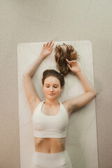 A girl in white clothes does yoga lying on a rug indoors