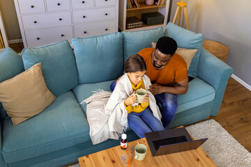 African American father and daughter with fever sitting at home and have online consultations with...