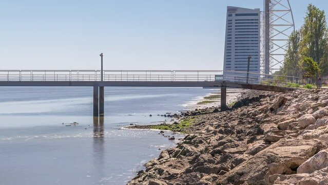 Motion from the low to high tide next to Vasco da Gama Bridge in Parque das Nacoes timelapse in Lisbon, Portugal. Level of water is rising up. Waterfront in Park of Nations district with skyscraper