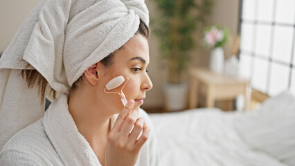 Young beautiful hispanic woman wearing bathrobe massaging face with skin gym at bedroom