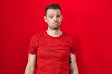 Young hispanic man standing over red background depressed and worry for distress, crying angry and...