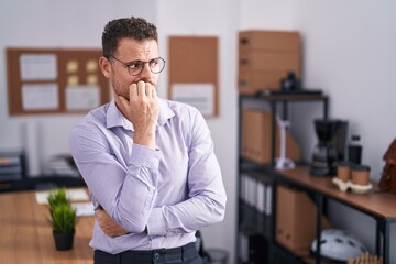 Young hispanic man at the office looking stressed and nervous with hands on mouth biting nails. anxiety problem.