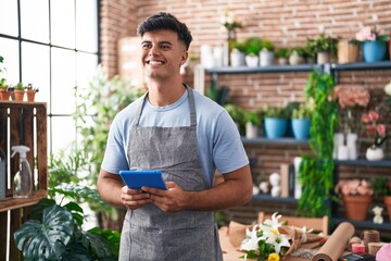 Young hispanic man florist smiling confident using touchpad at flower shop