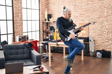 Middle age grey-haired man musician playing electrical guitar dancing at music studio