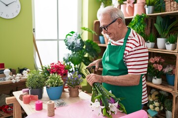 Middle age grey-haired man florist cutting stem at flower shop