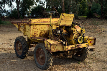 Close-up view of small beat up old yellow dumper truck. The vehicle with many scratches. Old rusty dumper track parked in a country side