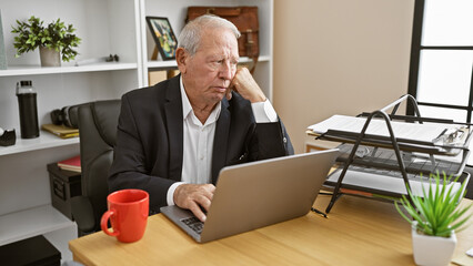 Serious, thoughtful senior man immersed in work, concentrating on business issues via laptop at office desk. a mature, elegant worker focused on success, doubting, crafting ideas and solutions.