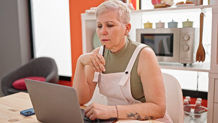 Fototapeta na wymiar Middle age grey-haired woman using laptop sitting on table with serious face at dinning room