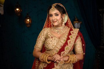 Stunning Indian bride dressed in traditional bridal lehenga with heavy gold jewellery and veil posing fashionable in studio lighting. Wedding fashion and lifestyle.