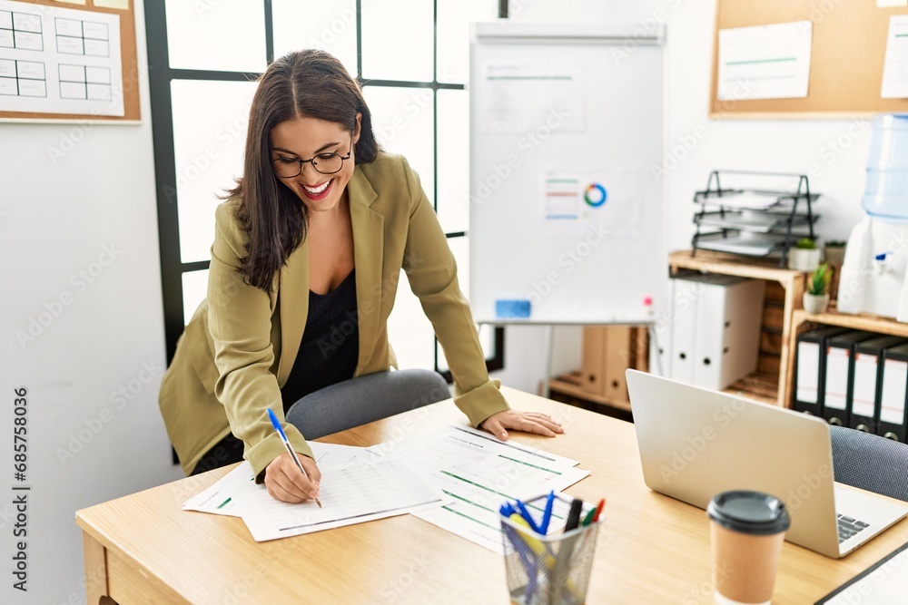 Wall mural Young beautiful hispanic woman business worker writing on document standing at office