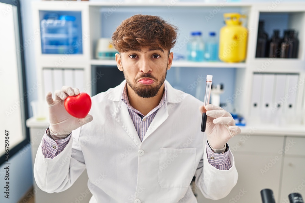 Poster arab man with beard working at scientist laboratory holding blood samples depressed and worry for di