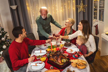 Grandfather is making a toast at the table. Family celebrating Christmas together eating homemade food.