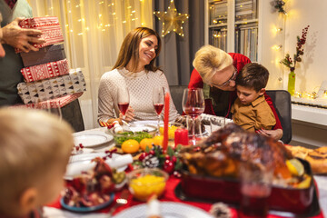 Grandparents giving presents to their grandchildren on Christmas Eve. Family having dinner.