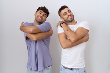 Homosexual gay couple standing over white background hugging oneself happy and positive, smiling confident. self love and self care