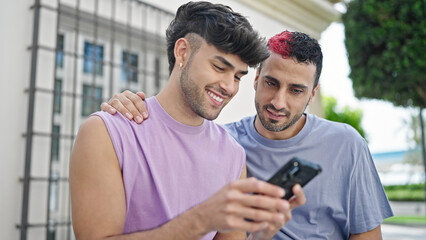 Two men couple smiling confident using smartphone at street