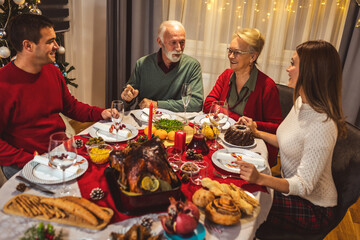 Happy family having Vhristmas dinner with their grandparents. Eating homemade food, drinking beverages. Home is decorated for New Year's Eve and Christmas