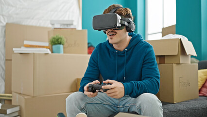 Young hispanic man playing video game using joystick and virtual reality glasses at new home