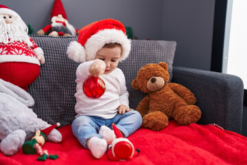 Adorable caucasian baby playing with christmas decoration ball sitting on sofa at home