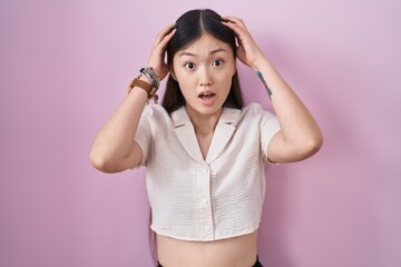 Chinese young woman standing over pink background crazy and scared with hands on head, afraid and surprised of shock with open mouth