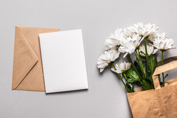 Craft envelope, blank form and bouquet of white chrysanthemums, daisies in a gift bag on a gray...