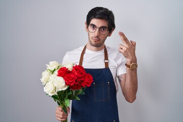 Young hispanic man holding bouquet of white and red roses shooting and killing oneself pointing hand and fingers to head like gun, suicide gesture.