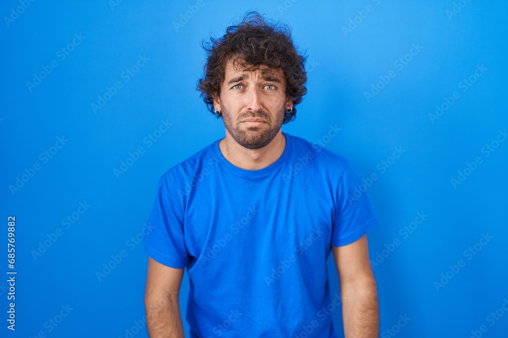 Wall mural Hispanic young man standing over blue background depressed and worry for distress, crying angry and afraid. sad expression.