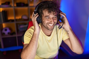 Young hispanic man streamer smiling confident sitting on table at gaming room