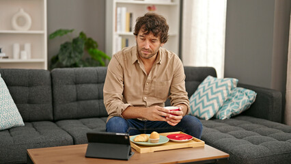 Young hispanic man having breakfast watching video on touchpad at home