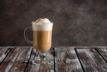 Cappuccino coffee with foam in a tall glass on a dark old wooden table. Side view, copy space.