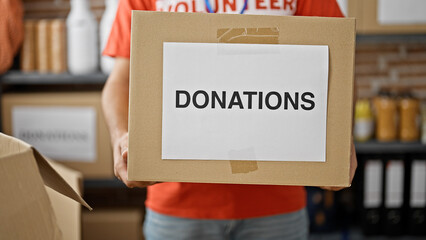 Young hispanic man volunteer holding donations cardboard box at charity center
