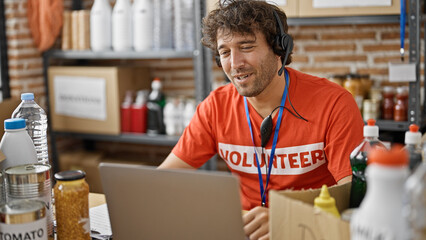 Young hispanic man volunteer writing on clipboard having video call at charity center