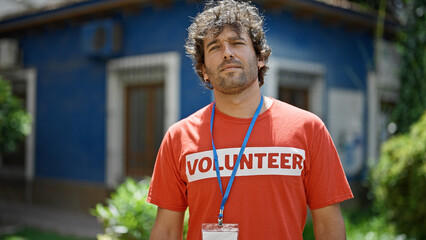Young hispanic man activist wearing volunteer uniform standing with serious face at park