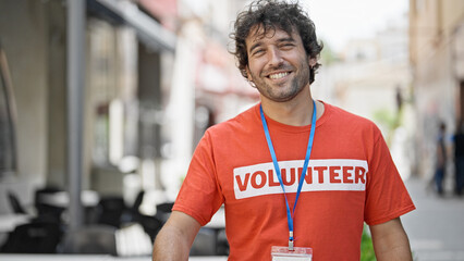 Young hispanic man activist wearing volunteer uniform smiling at street