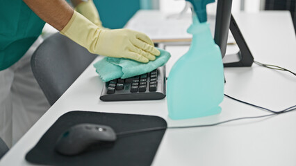 Young hispanic man cleaning keyboard with a cloth at office - Powered by Adobe